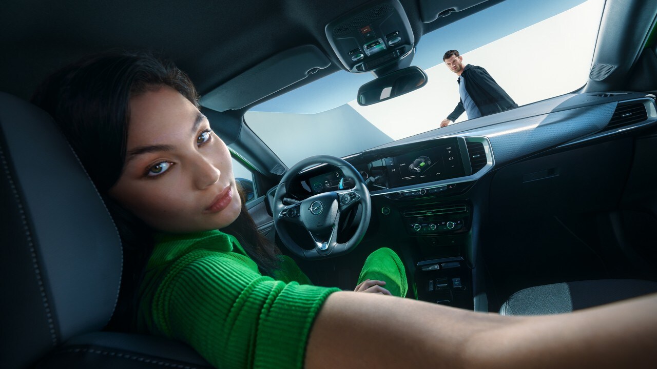 Woman looking back whilst in driver seat of an Opel Mokka Electric with a man walking outside